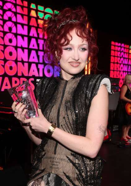 Chappell Roan in a black corset holding an award against a colorful background